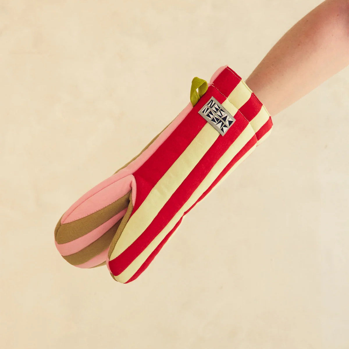 Striped Dusen Dusen oven mitt in pink, red, cream, and brown on hand