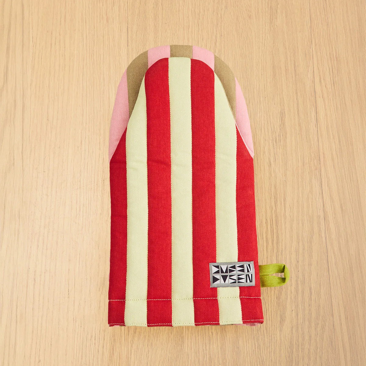 Striped Dusen Dusen oven mitts in pink, red, cream, and brown on wood background.