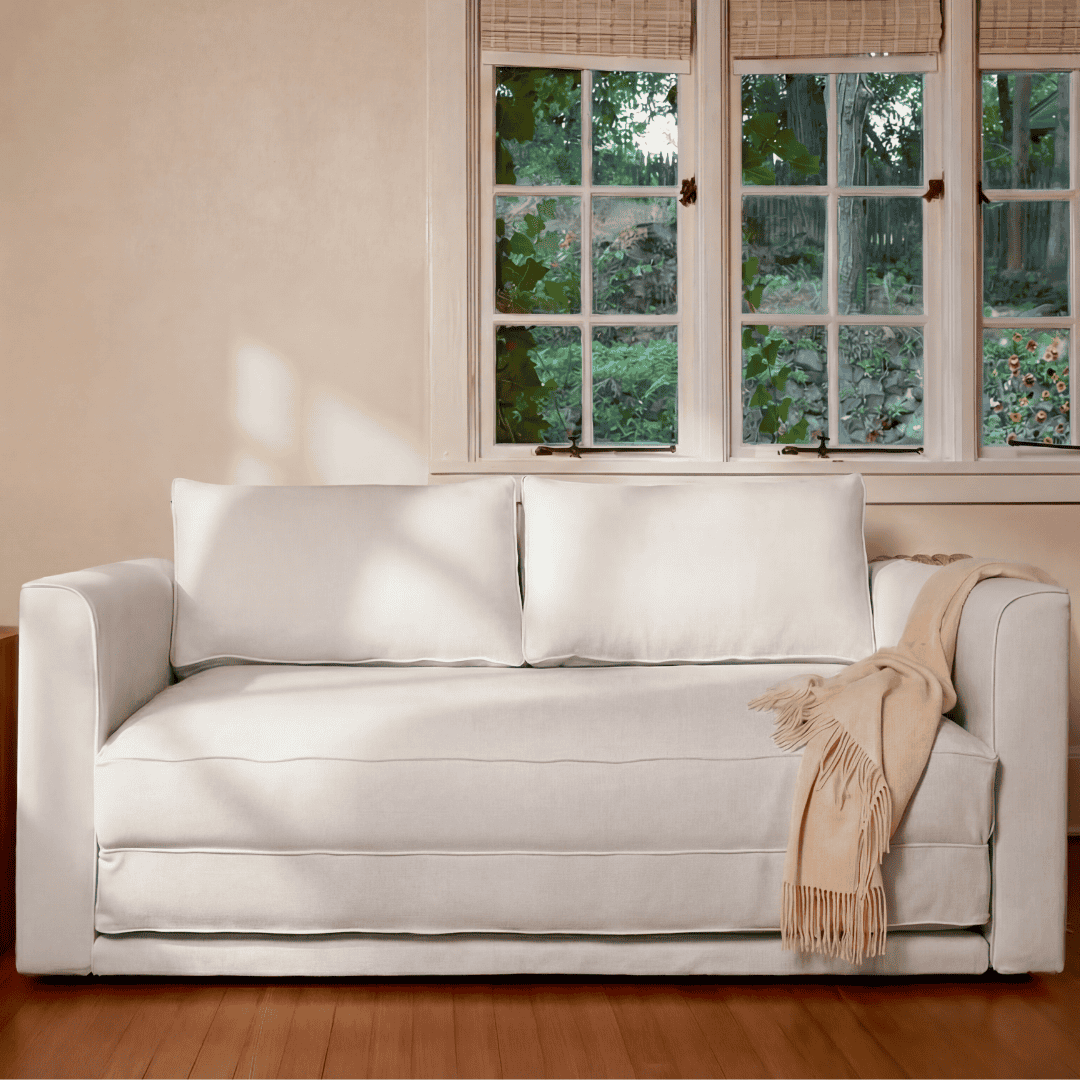 White sofa with a beige blanket in a room with a window and side table.